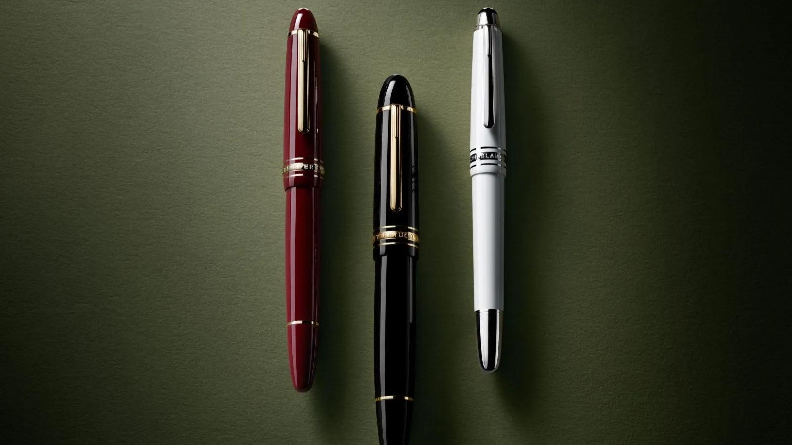 Trois stylos de luxe Montblanc Meisterstück en bordeaux, noir et blanc disposés côte à côte sur un fond vert foncé texturé.