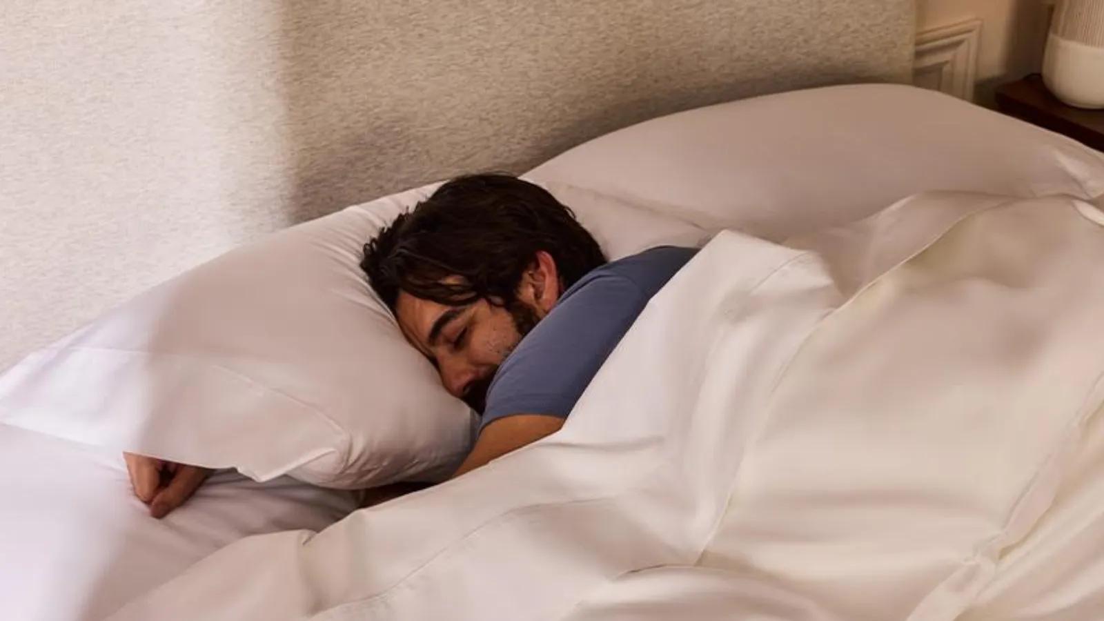 A man sleeping peacefully in a bed with white pillows and a white duvet.