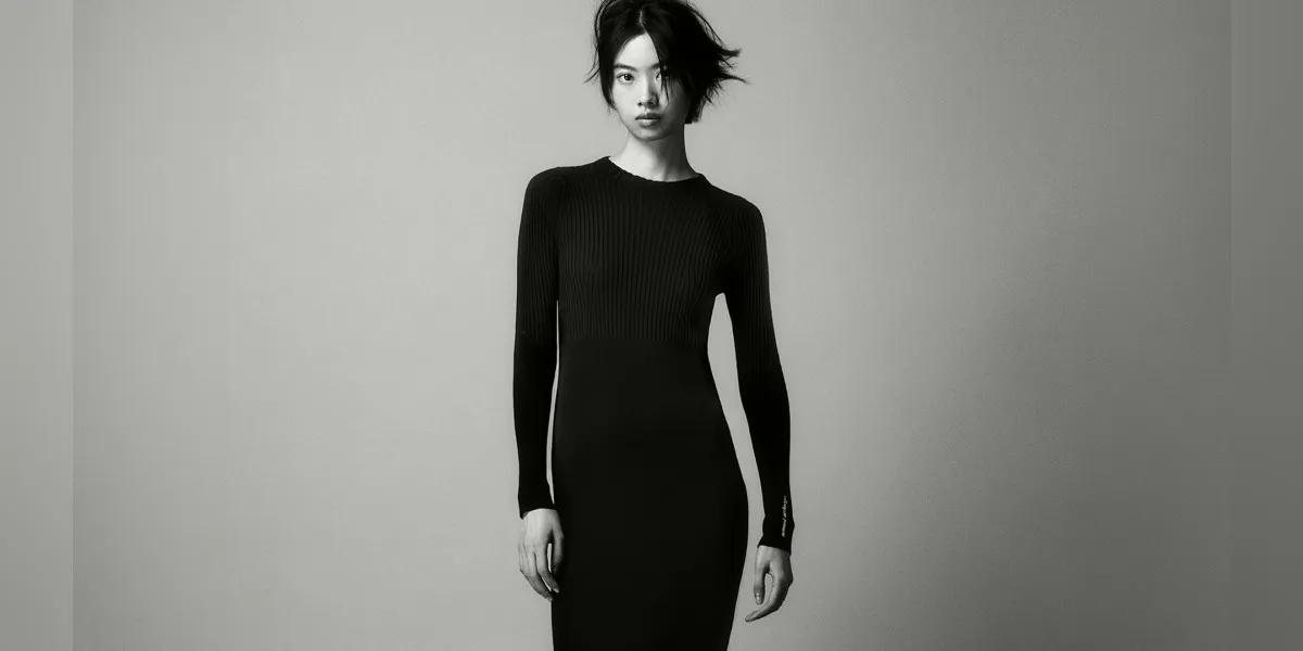Une photo en noir et blanc d'un mannequin portant une robe noire à manches longues sur un fond uni.