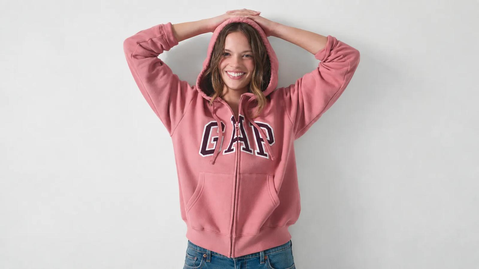 A smiling woman posing in a pink Gap zip-up hoodie with her hands resting on the hood.