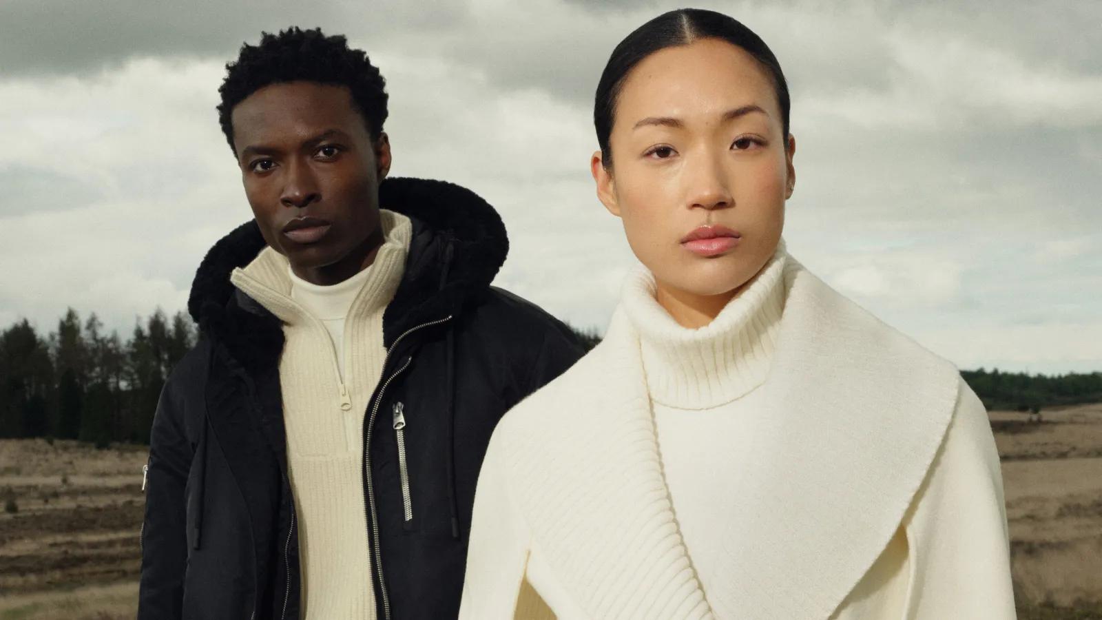 Two models wearing Mackage fall outerwear and cream knitwear outdoors under an overcast sky.