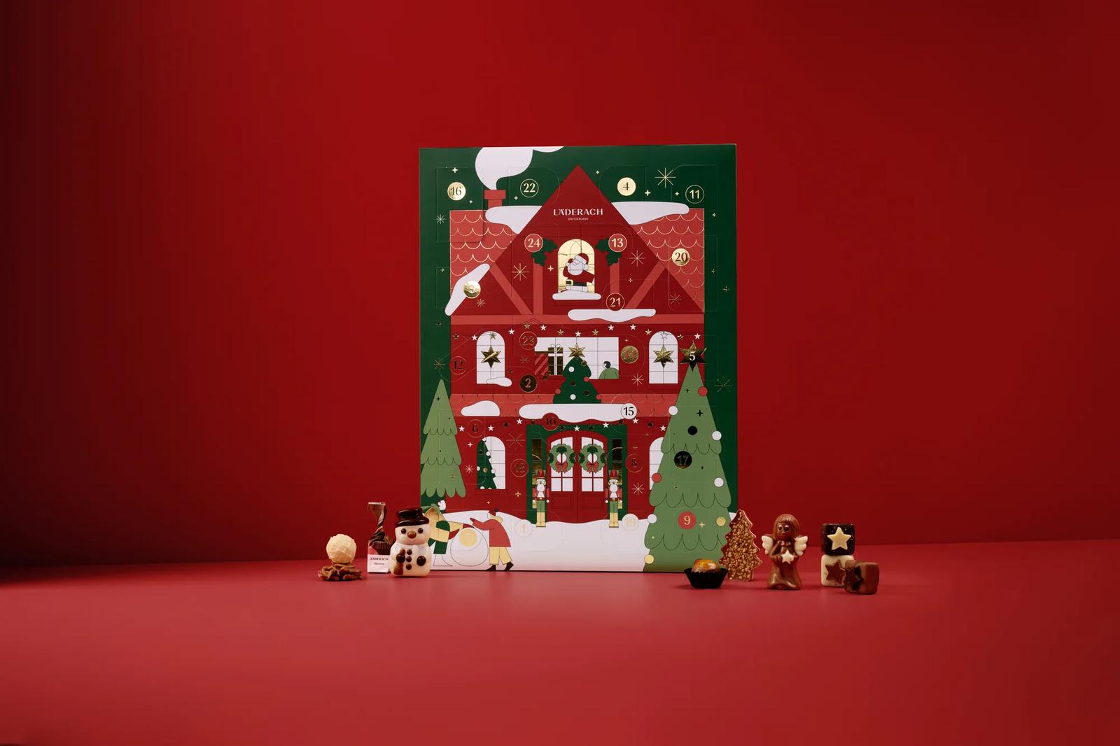 A Läderach house-shaped advent calendar surrounded by small chocolate figures on a solid red background.