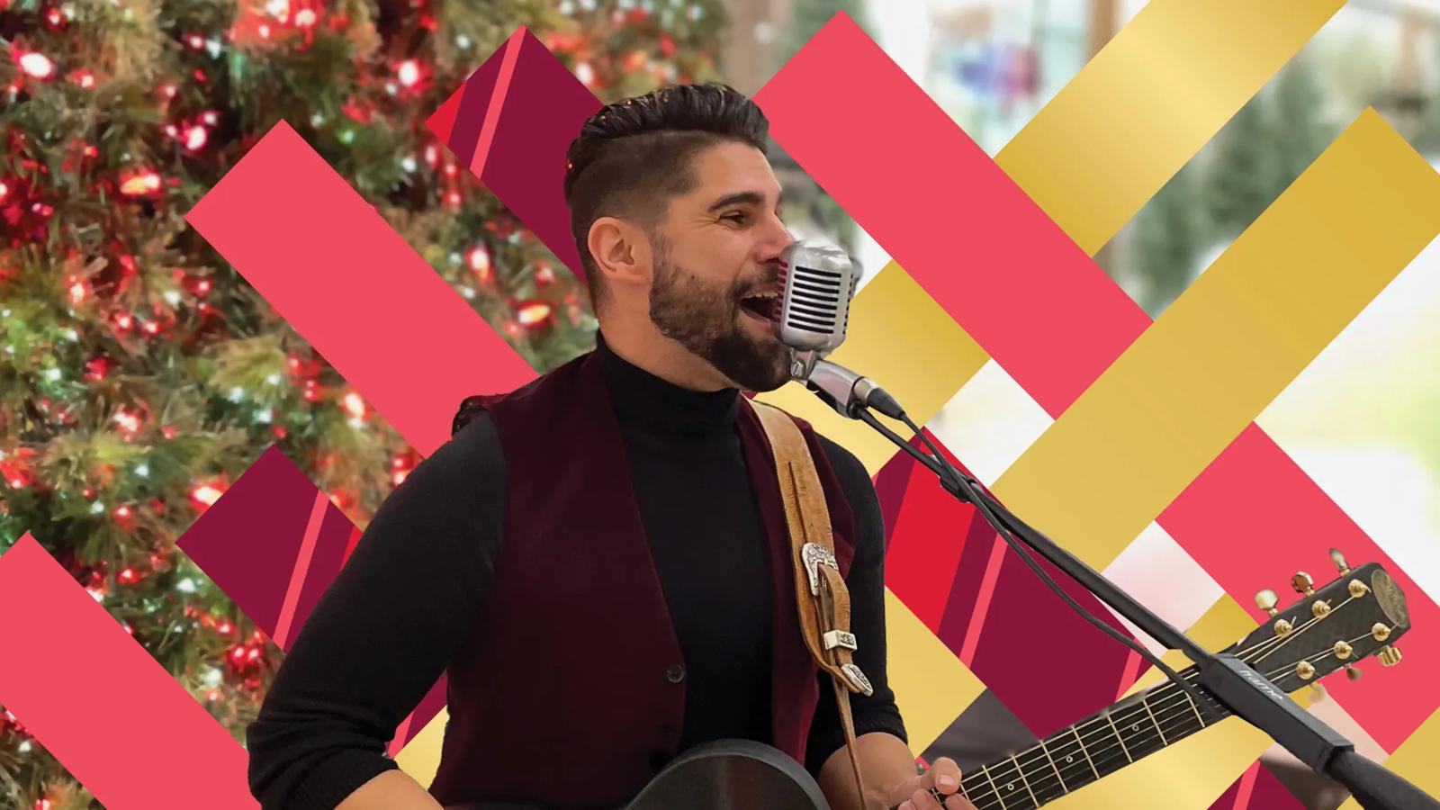 A guy singing and playing guitar in front of a Christmas tree in a festive setting