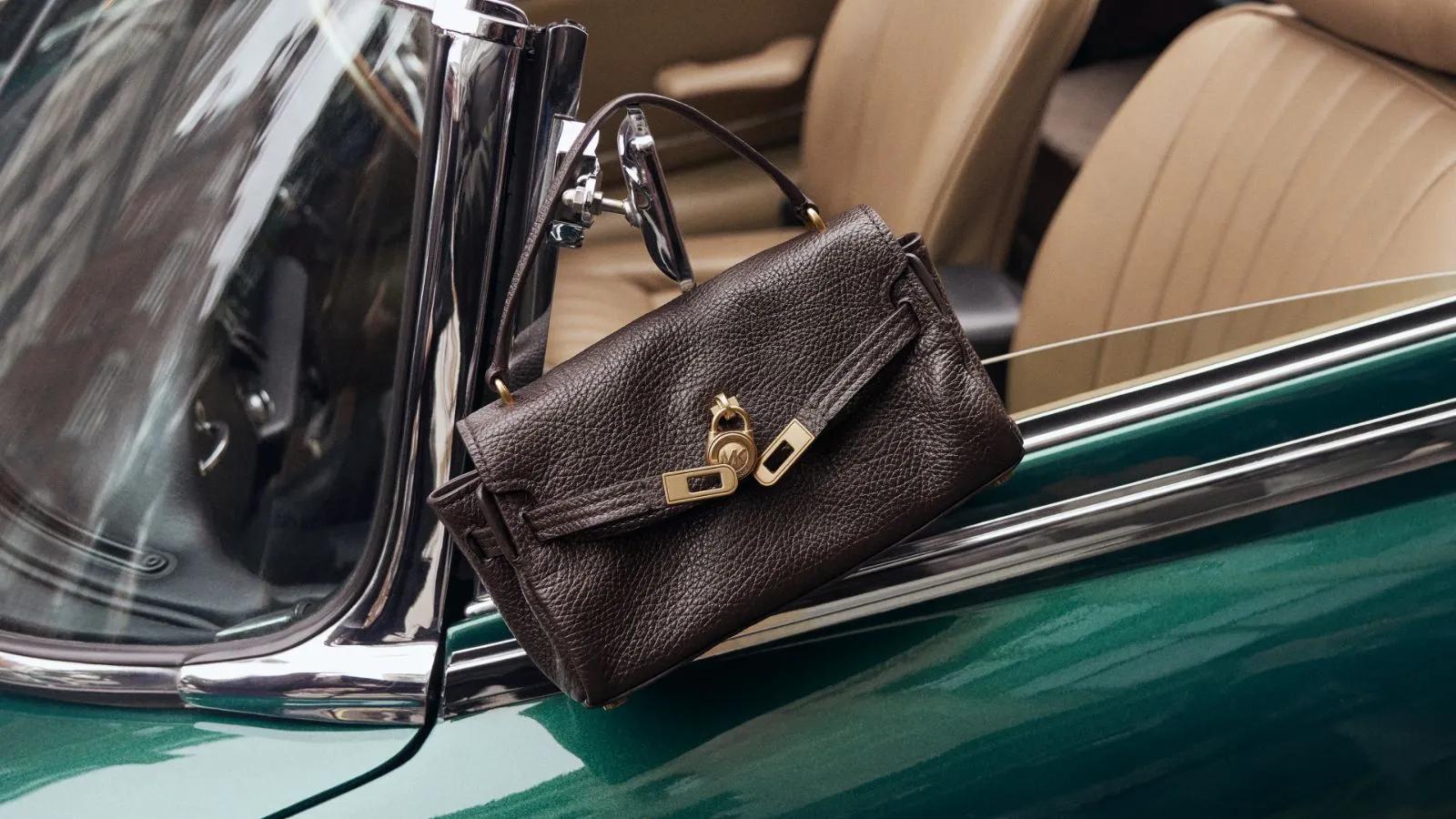 A dark brown Michael Kors leather handbag hanging from the side mirror of a classic green convertible car.