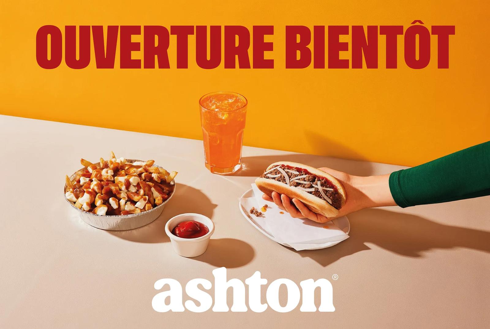 Une publicité Ashton indiquant « Ouverture Bientôt » avec une main tenant un hot-dog à côté d'un bol de poutine et d'une boisson glacée.