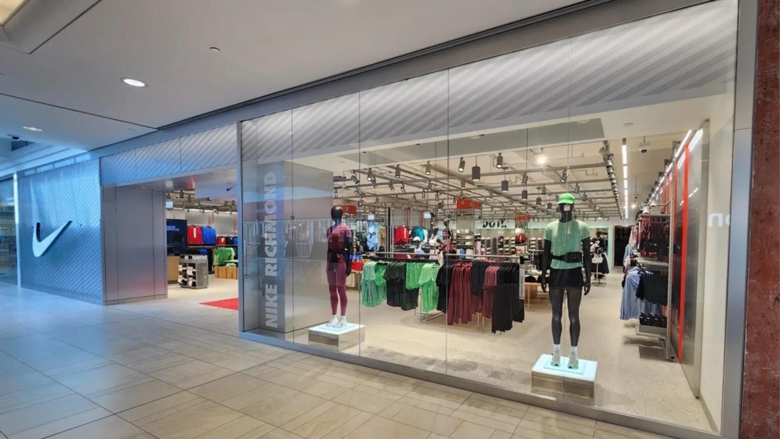 The storefront display of a Nike store featuring mannequins, apparel racks, and large glass windows.