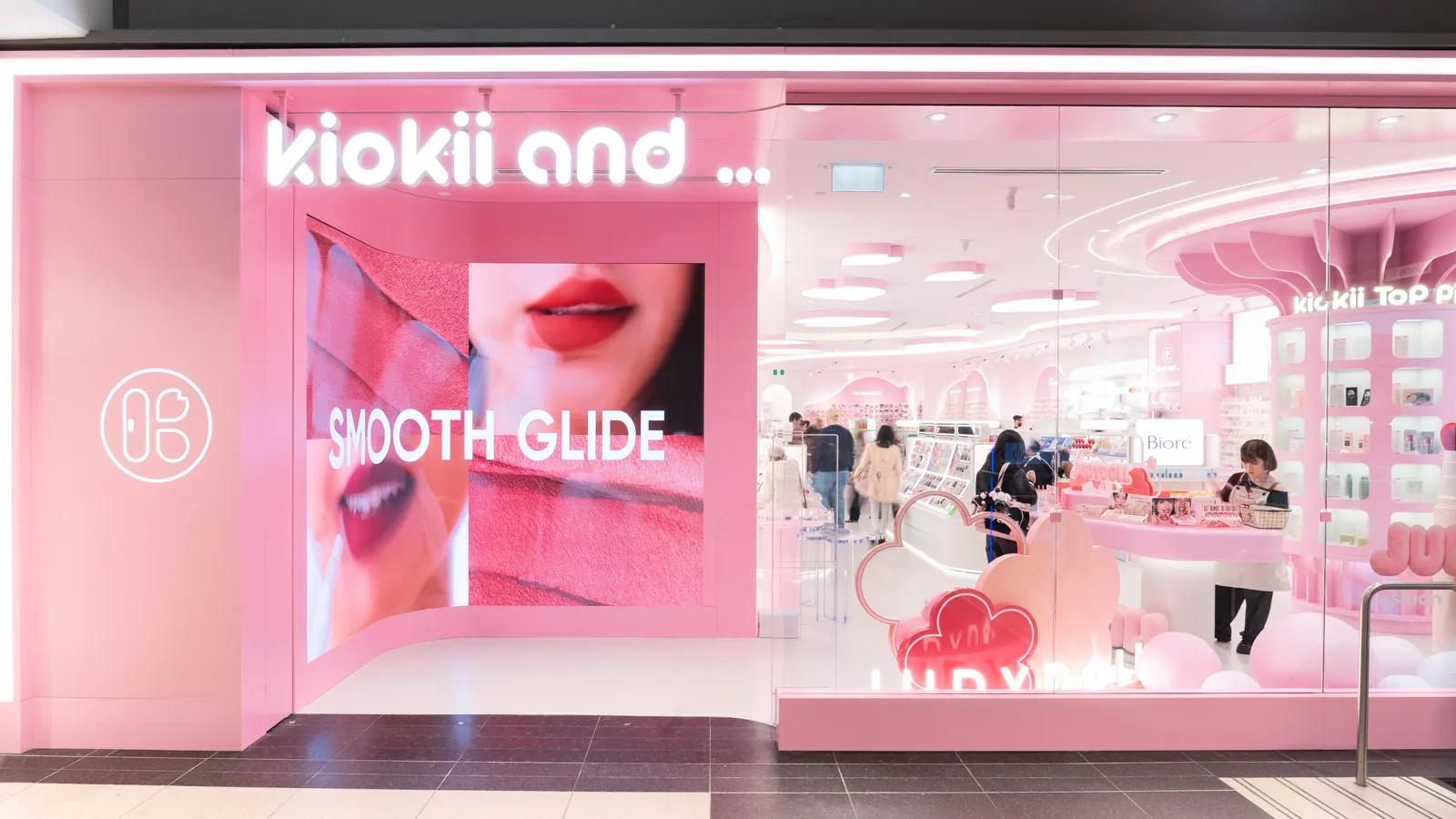 The bright pink storefront of a "kiokii and..." beauty store featuring a large digital display.