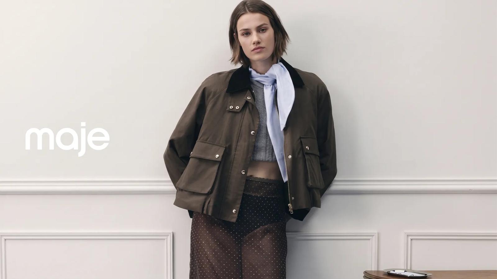 A Maje promotional image featuring a model wearing a dark top with a fur collar against a pink patterned couch.