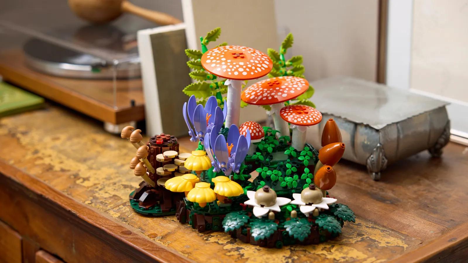 A built LEGO set featuring colorful mushrooms, purple flowers, and forest greenery displayed on a wooden surface.
